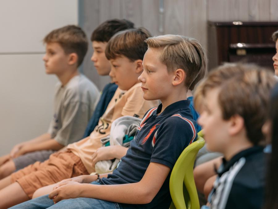 Die Kinder sitzen bei der Einschulung in der Mensa auf Stühlen und hören zu, wie Reden gehalten werden. 