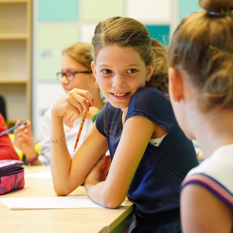 Mehrer junge Schülerinnen sitzen gemeinsam im Klassenraum, sie unterhalten sich und  lächeln sich an. 