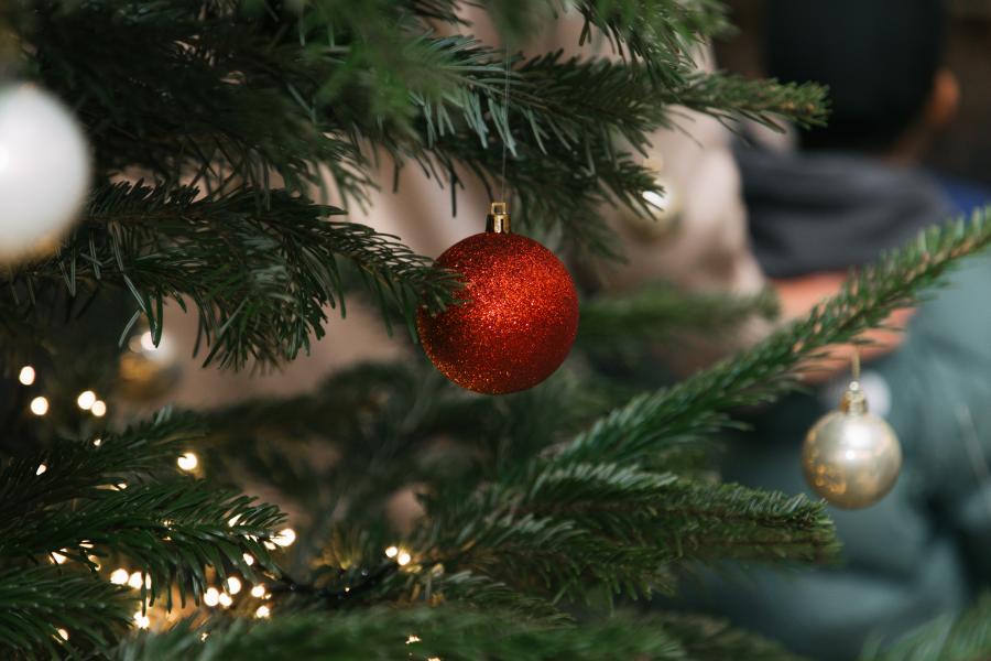 Zu sehen ist ein Zweig des festlich geschmückten Weihnachtsbaums mit Lichtern und Christbaumkugeln. 
