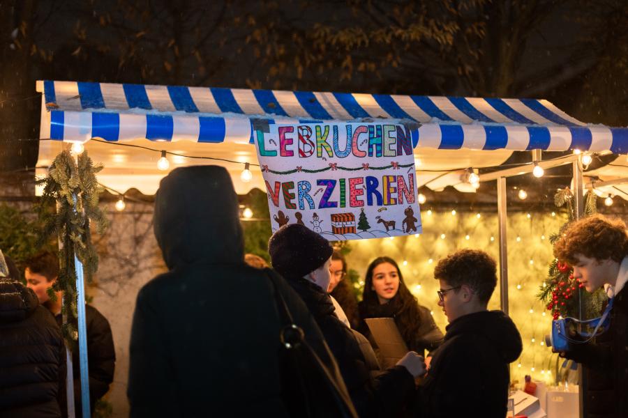 Ein verzierter Stand am Weihnachtsmarkt, der von Schülern geführt wird. Auf einem Schild steht "Lebkuchen verzieren"