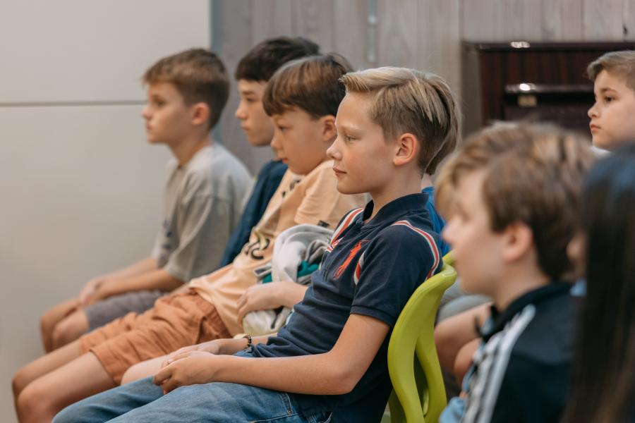 Die Kinder sitzen bei der Einschulung in der Mensa auf Stühlen und hören zu, wie Reden gehalten werden.